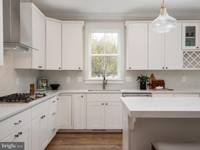 kitchen featuring a sink, white cabinetry, stainless steel appliances, crown molding, and wall chimney range hood