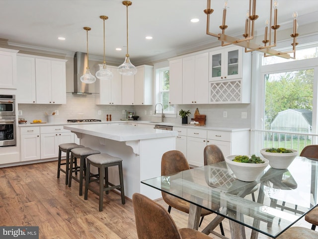 kitchen featuring light wood finished floors, ornamental molding, light countertops, wall chimney exhaust hood, and a center island