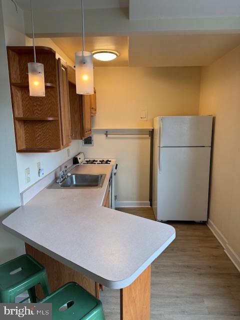 kitchen with light wood-type flooring, light countertops, a peninsula, freestanding refrigerator, and a sink