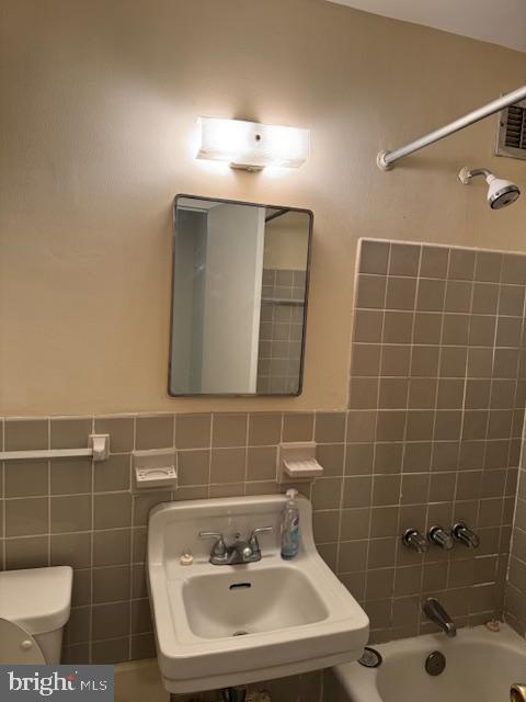 bathroom with tile walls, toilet, shower / bathtub combination, and a sink