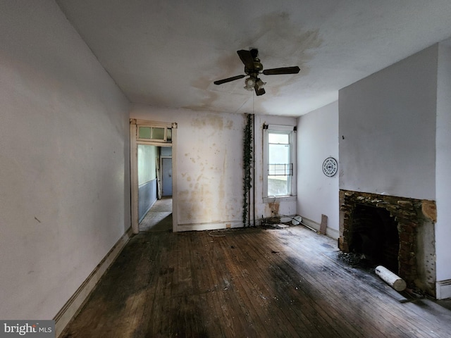 unfurnished living room with baseboards, wood-type flooring, a stone fireplace, and a ceiling fan