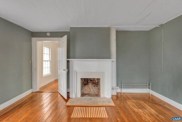 unfurnished living room with hardwood / wood-style floors, a fireplace with flush hearth, and baseboards