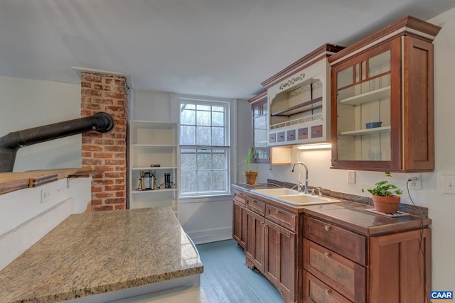 kitchen featuring a sink, open shelves, wood finished floors, brown cabinetry, and glass insert cabinets