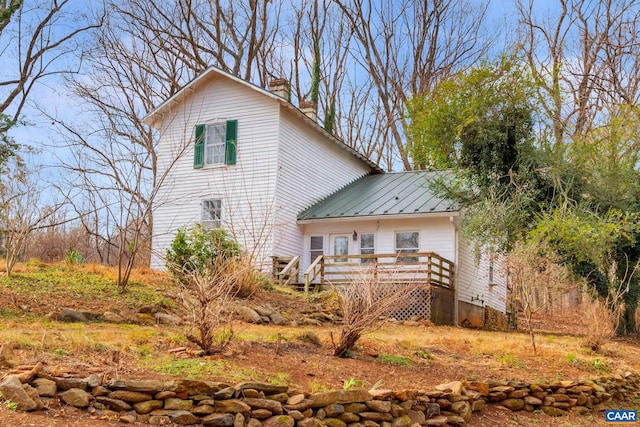 back of house featuring a standing seam roof, a wooden deck, metal roof, and a chimney