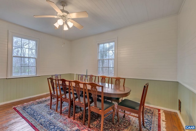 dining area with a wainscoted wall, a healthy amount of sunlight, a ceiling fan, and wood finished floors