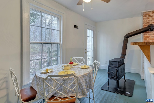 dining space with hardwood / wood-style flooring, a wood stove, a ceiling fan, and baseboards