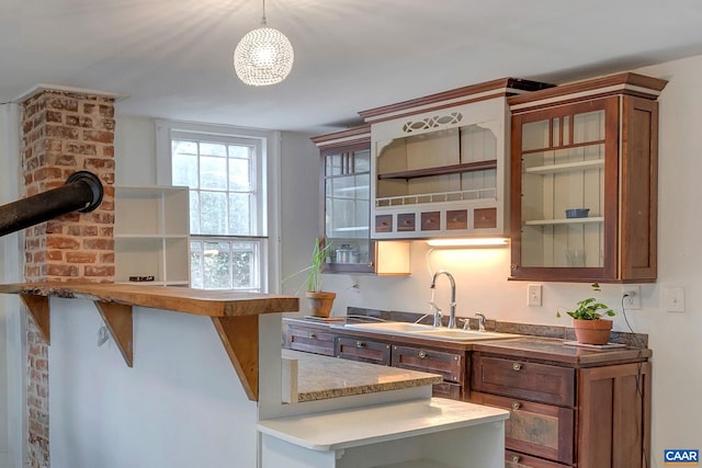 kitchen featuring open shelves, a sink, glass insert cabinets, decorative light fixtures, and brown cabinets