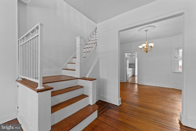 stairs featuring hardwood / wood-style floors, a notable chandelier, and baseboards