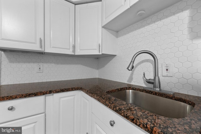 kitchen with tasteful backsplash, dark stone countertops, white cabinetry, and a sink