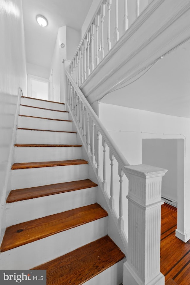 stairway featuring a baseboard heating unit and wood finished floors