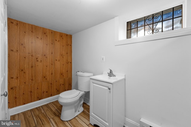 bathroom featuring baseboard heating, wood walls, toilet, and wood finished floors