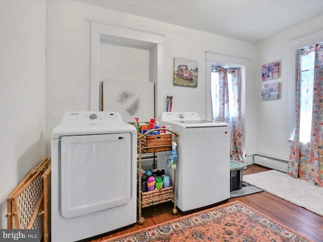 laundry room featuring a baseboard heating unit, wood finished floors, washing machine and dryer, and a wealth of natural light