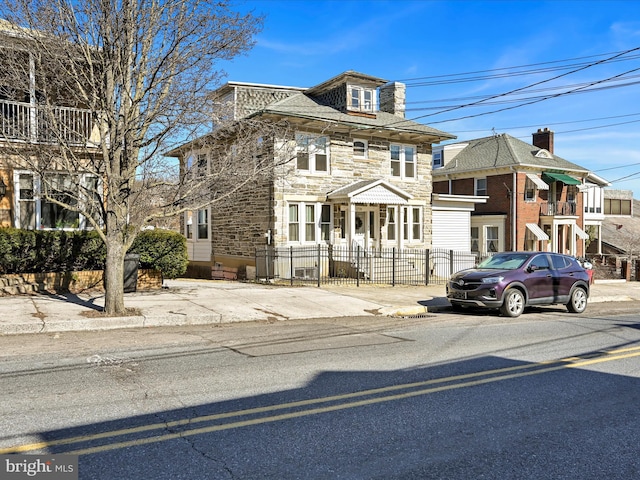 american foursquare style home with a fenced front yard and stone siding