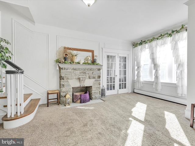 living room with a baseboard heating unit, french doors, carpet, a stone fireplace, and a decorative wall