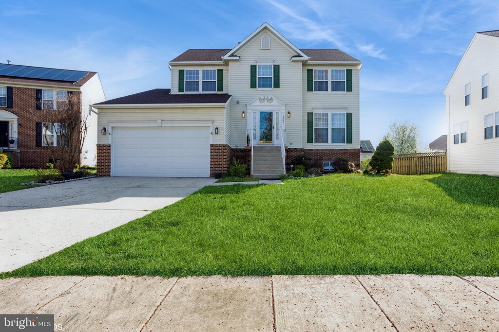 view of front of property featuring brick siding, concrete driveway, fence, and a front lawn