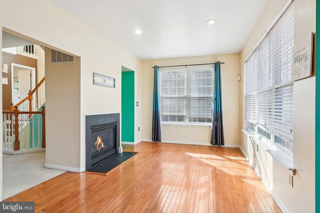 107 Persimmon Pl, Bear, DE 19701 - unfurnished living room featuring wood-type flooring, plenty of natural light, a glass covered fireplace, and stairs