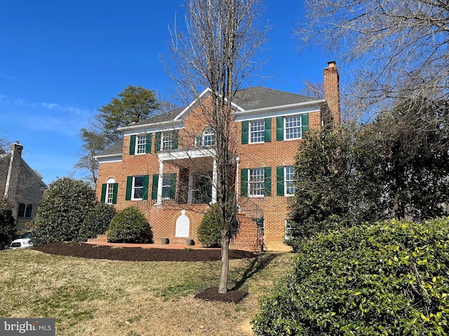 colonial house featuring brick siding, a chimney, and a front lawn