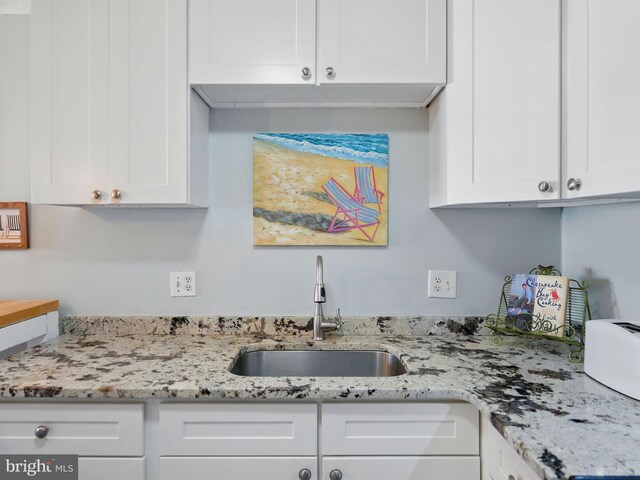 kitchen with a sink, light stone countertops, and white cabinets