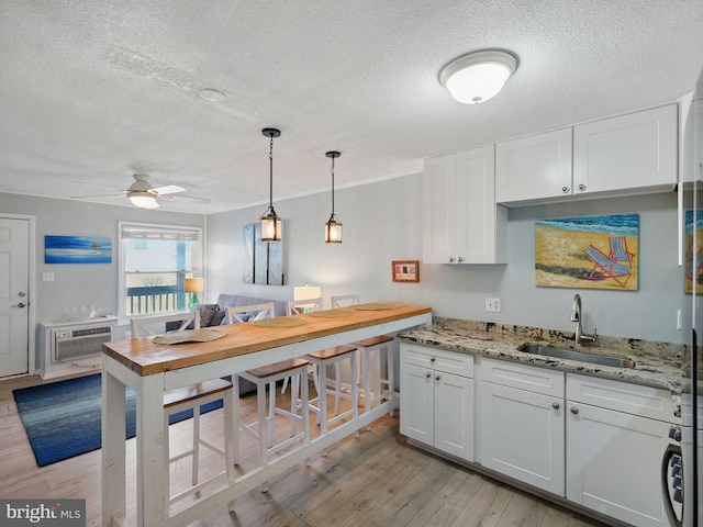 kitchen with light wood-type flooring, light stone counters, white cabinets, a wall mounted AC, and a sink