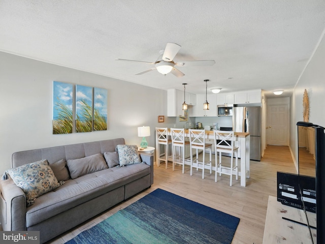 living area with light wood-type flooring, a textured ceiling, and ceiling fan