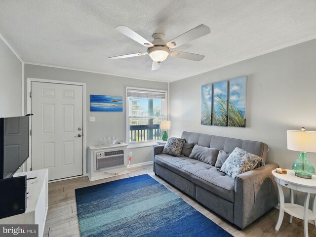 living room with a wall mounted AC, ornamental molding, ceiling fan, a textured ceiling, and light wood-type flooring