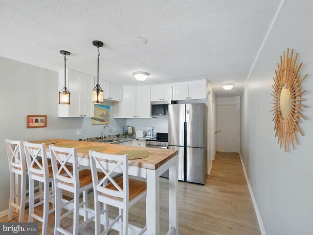 kitchen featuring butcher block countertops, light wood-style flooring, a sink, appliances with stainless steel finishes, and a peninsula