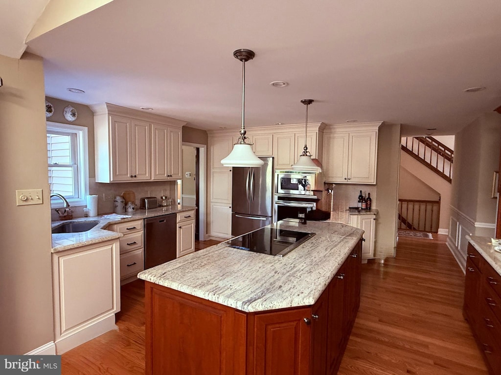 kitchen with a sink, a kitchen island, wood finished floors, stainless steel appliances, and light stone countertops