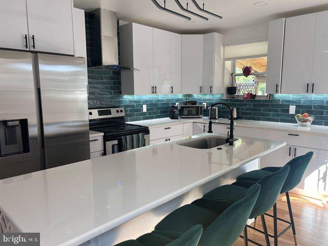 kitchen featuring wall chimney range hood, a breakfast bar area, appliances with stainless steel finishes, and a sink