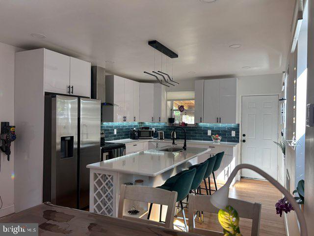 kitchen featuring wall chimney range hood, stainless steel fridge with ice dispenser, light countertops, range with electric stovetop, and a sink