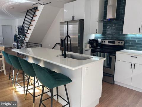 kitchen with a breakfast bar, light wood-style flooring, stainless steel appliances, wall chimney exhaust hood, and tasteful backsplash