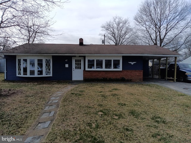 ranch-style home featuring brick siding, an attached carport, a front yard, a chimney, and driveway