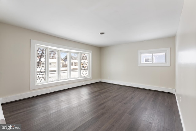 empty room with dark wood finished floors, plenty of natural light, baseboard heating, and baseboards