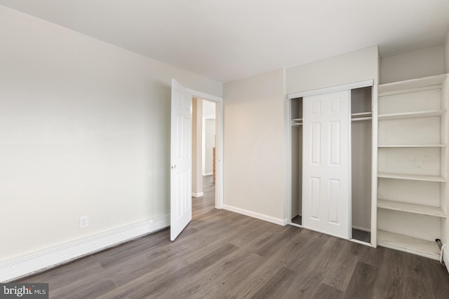 unfurnished bedroom with a baseboard radiator, baseboards, a closet, and wood finished floors