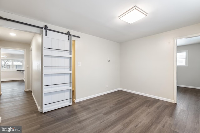 empty room featuring a barn door, baseboards, and dark wood-style flooring