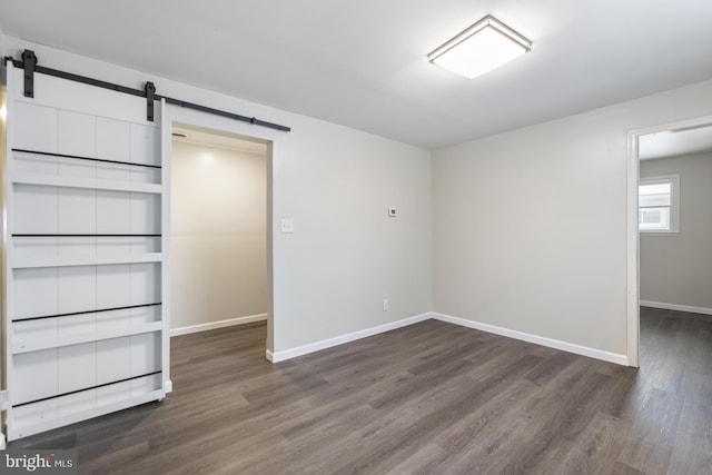 unfurnished bedroom with dark wood finished floors, a barn door, and baseboards