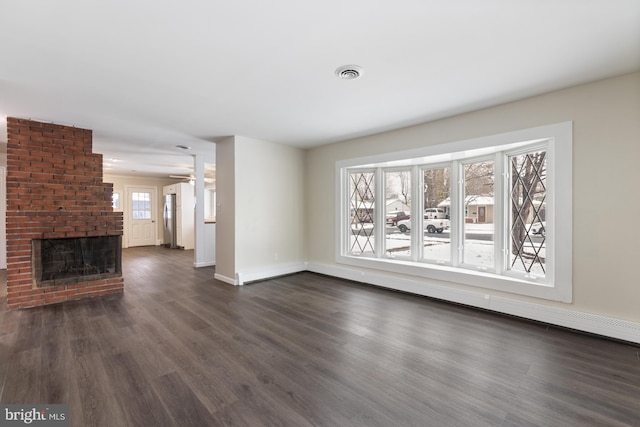 unfurnished living room featuring a brick fireplace, plenty of natural light, dark wood-style floors, and visible vents