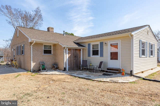 rear view of property with entry steps, roof with shingles, brick siding, a chimney, and a patio area