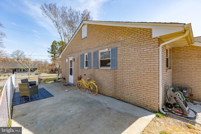 view of side of home featuring fence, a patio area, and brick siding