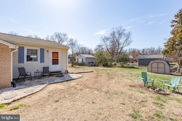 view of yard featuring entry steps, an outdoor structure, a storage unit, and a fire pit