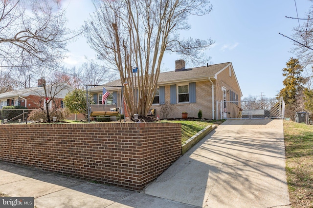 view of front of home featuring driveway, a gate, fence, brick siding, and a chimney