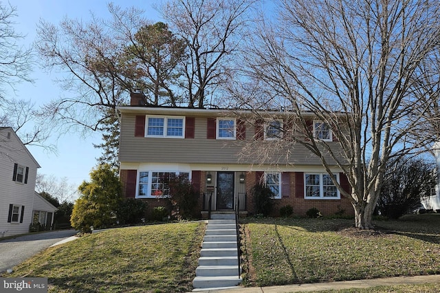 colonial home with a front yard, brick siding, and a chimney