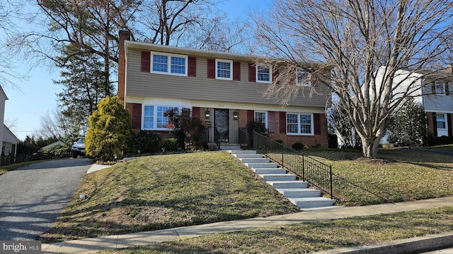 colonial inspired home with brick siding, driveway, a chimney, and a front yard