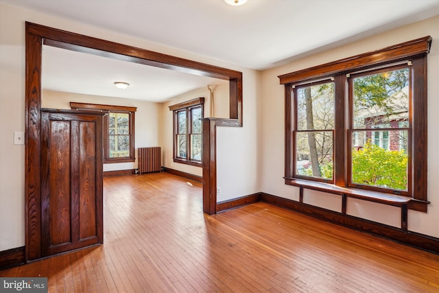 unfurnished room with light wood finished floors, radiator, and baseboards