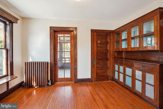 unfurnished room featuring hardwood / wood-style floors, radiator, a healthy amount of sunlight, and baseboards