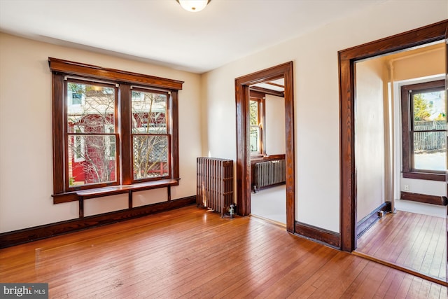 empty room featuring baseboards, radiator, and hardwood / wood-style flooring