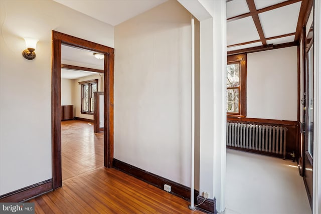 hallway featuring coffered ceiling, baseboards, radiator, and hardwood / wood-style flooring