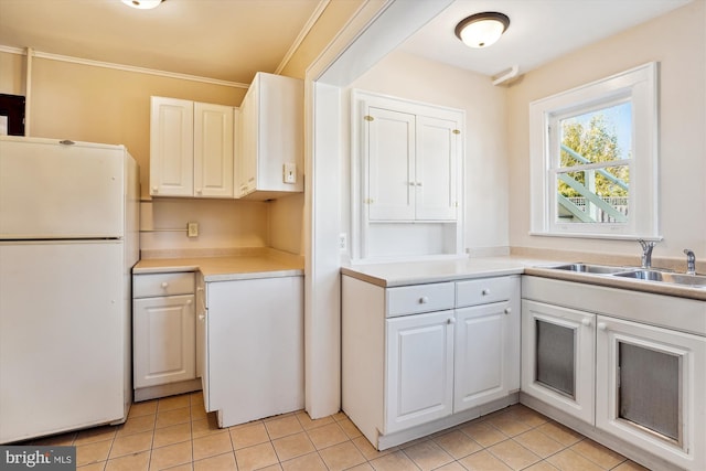 kitchen featuring light countertops, light tile patterned floors, freestanding refrigerator, white cabinetry, and a sink