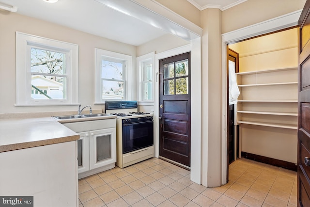 kitchen with white gas stove, light tile patterned flooring, ornamental molding, a sink, and white cabinets