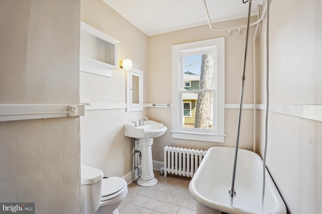 bathroom featuring tile patterned flooring, radiator, toilet, a soaking tub, and a sink