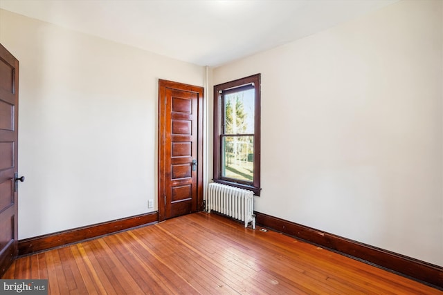 empty room featuring hardwood / wood-style flooring, radiator, and baseboards